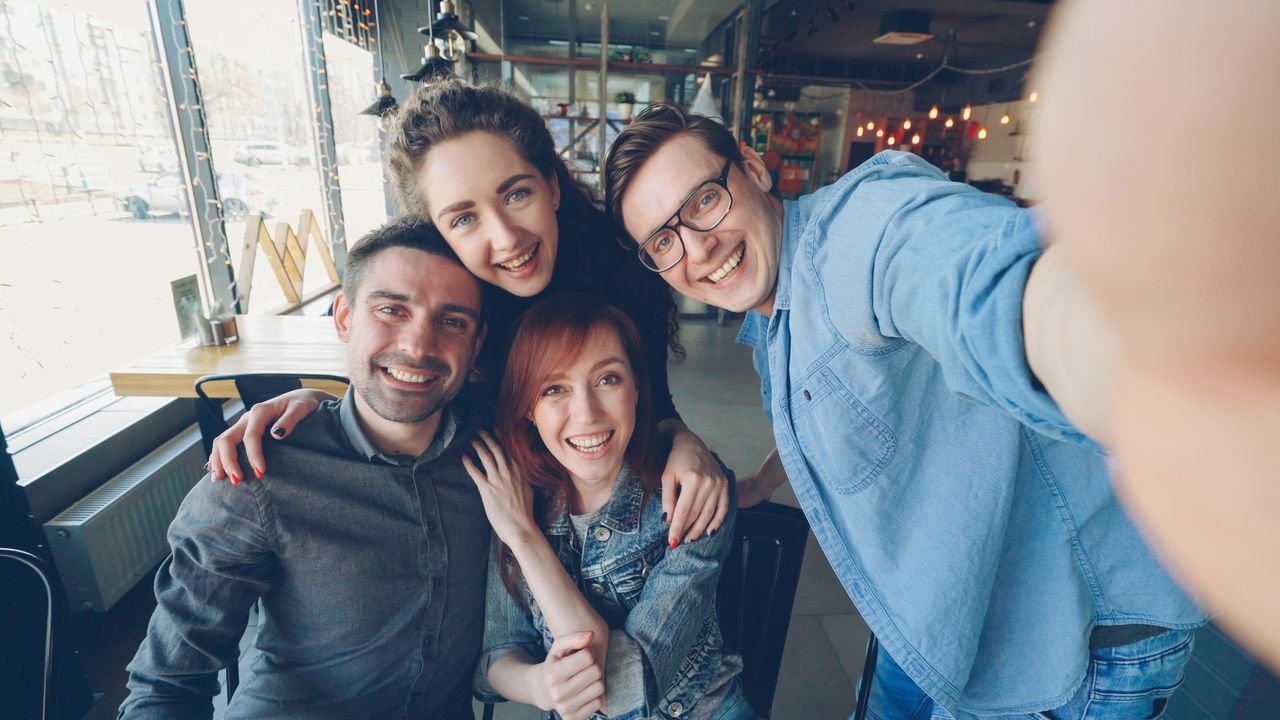 Happy group of friends taking a selfie together in a cozy cafe setting.
