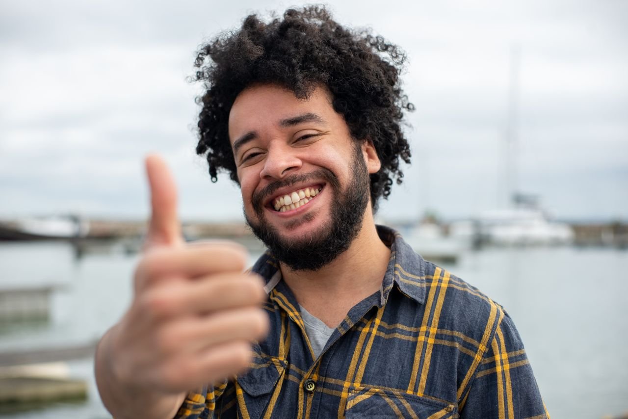 Happy man with a thumbs up gesture by the marina, expressing satisfaction and positivity.